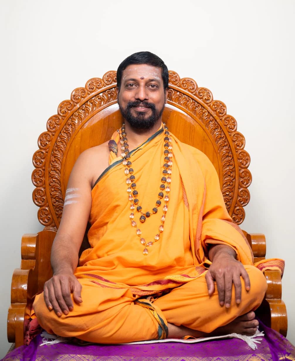 Paramapoojya Shri Shri Shri Maruthi Guruji seated in saffron robes on a carved wooden chair